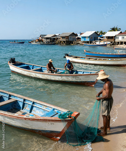 Authentic fishing village by the sea with colorful boats, local fishermen repairing nets, crystal-clear water, and bright summer light, realistic documentary travel photography