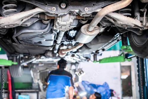 Obraz na płótnie Selective focus to automotive mechanic and detailed view of a vehicle's undercarriage, rear suspension, exhaust system, and rear differential raised on a hydraulic lift in an auto repair workshop