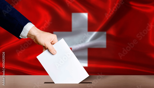 Foto Hand placing a ballot in ballot box with the Swiss flag in the background