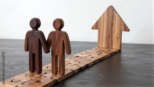 Two wooden figures walk puzzle path toward house, symbolizing shared journey to home.
