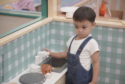 Canvastavla Asian toddler boy roleplaying at toy kitchen sink washing fake food items