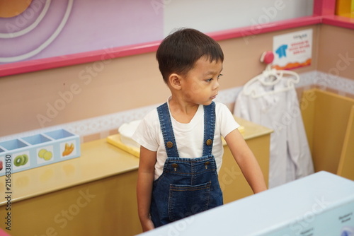 Foto Cute Asian toddler boy playing cashier at indoor playground bakery counter