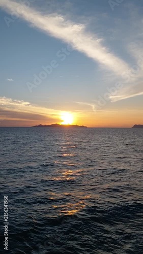 Golden sunset over the calm ocean with island silhouette and dramatic clouds reflecting on the water surface.