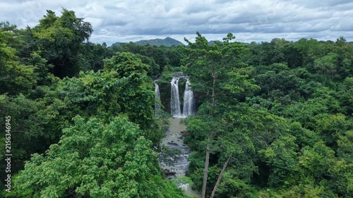 Cinematic drone footage flying directly toward a spectacular waterfall with three separate streams cascading down in white torrents. 