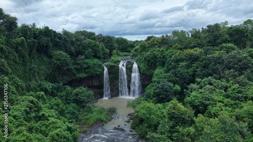 Cinematic drone footage flying directly toward a spectacular three-stream waterfall, moving closer to the cascading white water for an immersive close-up perspective. 