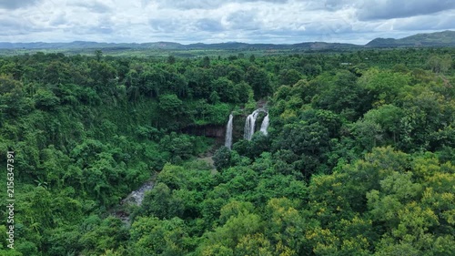 Cinematic drone footage orbiting around a spectacular three-stream waterfall, gradually revealing the surrounding pristine forest and untouched natural landscape. 