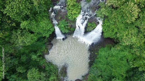 Cinematic drone footage starting with a top-down view of a spectacular three-stream waterfall. The camera gradually descends toward the waterfall before smoothly tilting upward into a horizontal front