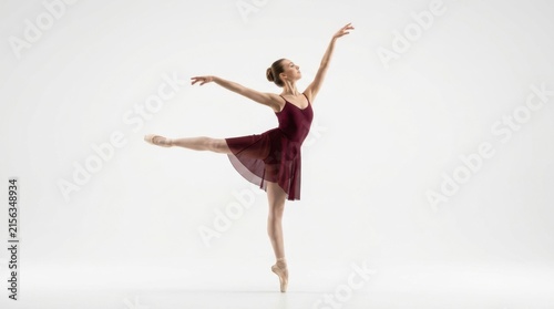 Graceful young ballerina in a dark red dress performing a beautiful ballet dance pose on her toes in the studio