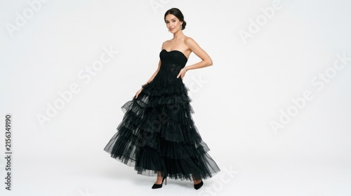 Elegant young woman wearing a long black strapless tulle evening gown standing and posing gracefully for a fashion shoot