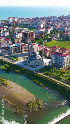 Vertical video. Ardeshen, Turkey. Ensar Mosque with twin minarets and large central dome, aerial view over the Firtina River estuary on a bright sunny morning with the Black Sea beyond. Aerial View, 