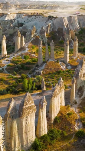 Vertical video. Goreme, Nevsehir, Turkey. Love Valley fairy chimneys, tall volcanic tuff pillars with dark basalt capstones, aerial view at golden hour over the eroded Cappadocian landscape. Aerial V