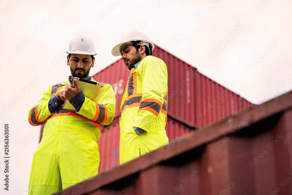 Fototapeta premium Logistics engineers resting and talking on top of cargo container at freight yard. Workplace Break, Container Logistics, Freight Terminal, Teamwork, Industrial Inspection