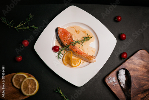 Grilled salmon steak with lemon slices and fresh rosemary elegantly arranged on a white plate with premium food styling. Sophisticated gourmet seafood presentation photographed from above