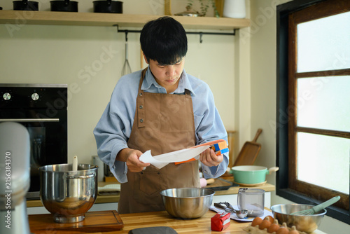 Fotografía Young Asian Man Preparing Parchment Paper for Cookie Baking in Home Kitchen
