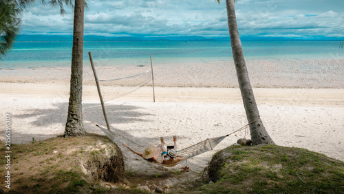 Top view of couple tourist are in motion of relaxing stay under coconut palm tree at the the edge of the sea beach,  trip summer on vacation of couple lover