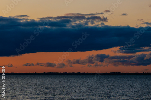 Canvastavla Sunset over calm water with dark clouds and vibrant orange and blue hues reflect