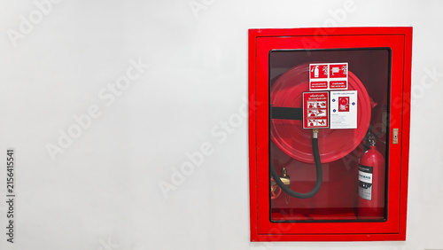 Wall Mounted Fire Hose Reel: A bright red, wall-mounted fire hose reel housed in a protective glass-fronted cabinet, ready for emergency use. Fire safety equipment cabinet with copy space.