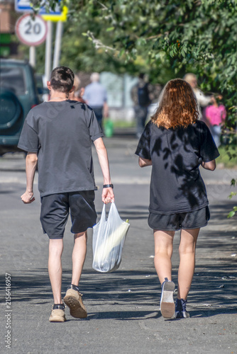 A man and a woman with shopping are walking along the sidewalk on a summer day