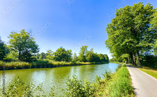 Cuadro en lienzo bright summer towpath alongside green canal under clear blue sky
