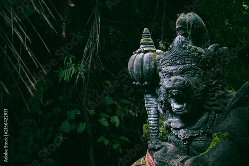 Balinese stone guardian statue stands with an open mouth and fierce expression. Its intricate monkey-like carving covered in moss