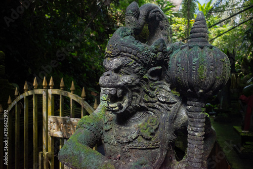 Stone monkey statue representing Hanuman, a Hindu deity, standing guard at a moss-covered temple entrance in Bali, Indonesia, symbolizing protection and ancient culture