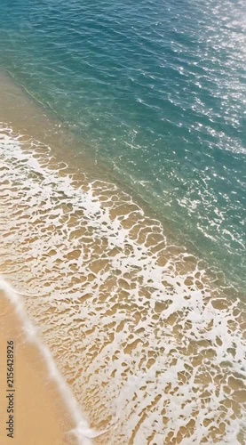 Aerial View of Gentle Ocean Waves Lapping Against Sandy Beach Under Bright Sunlight