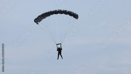 Konstfotografi Paratrooper Descending with a Black Parachute Against a Pale Sky