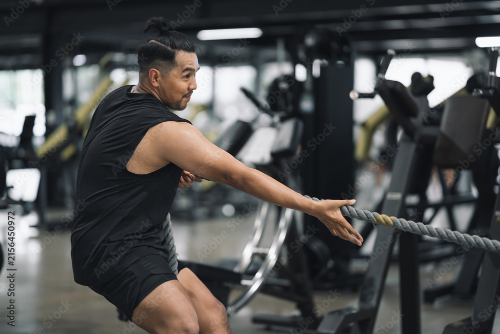 Fototapeta premium Man performing battle rope exercise or exercise with sled pull in gym