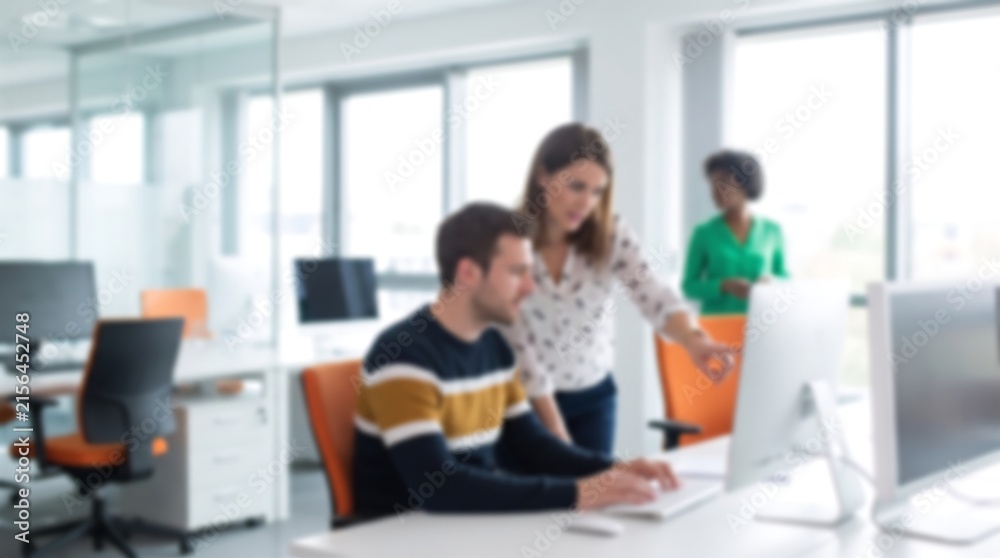 Fototapeta premium Professional colleagues working together in bright modern office space with computer monitors and orange chairs blurred for creative background copy space and business focus