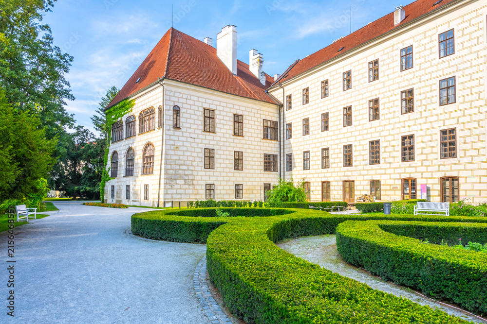 Obraz premium Visitors walk near Trebon Castle in Trebon, Czech Republic. The castle features historic architecture and well-kept gardens. People enjoy the outdoor space and the beauty of this site.