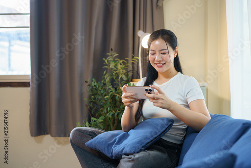 Smiling relaxed young woman sitting on couch using cell phone technology, happy lady holding smartphone, scrolling, looking at cellphone enjoying doing online e commerce shopping in mobile apps.