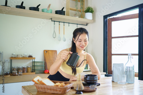 Bild auf Leinwand Young Asian Woman in Workout Clothes pouring hot water into matcha bowl in modern kitchen