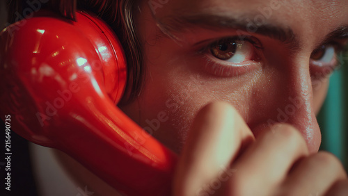 Close-up of a person holding a red vintage telephone receiver to their ear.