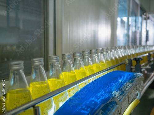 Rows of glass bottles filled with yellow liquid on a factory production line, showcasing automated beverage manufacturing, quality consistency, and industrial food processing in a clean facility.