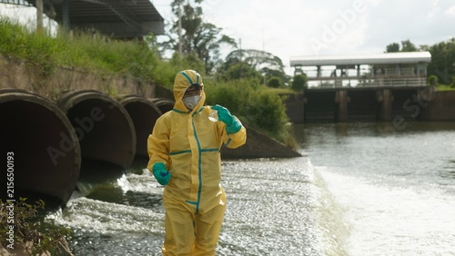 Fotografía Scientist in Yellow Hazmat Suit Holding Flask Inspecting Water Sample Turbidity