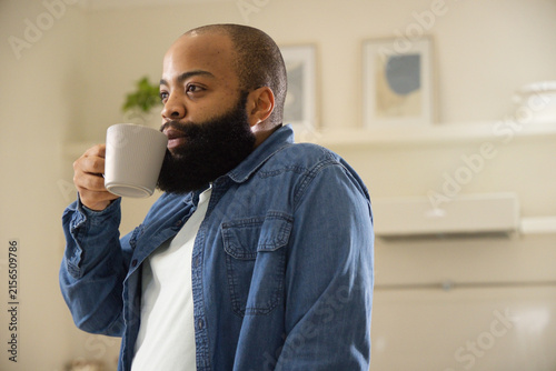 African American man wearing denim shirt, white T-shirt standing in kitchen holding ribbed mug