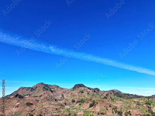 Expansive mountain panorama with terraced agricultural fields under bright clear blue sky and thin cloud