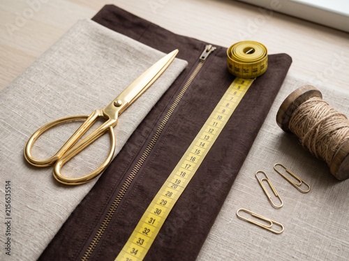 Vintage golden brass scissors resting on beige linen fabric alongside a yellow measuring tape and sewing supplies.