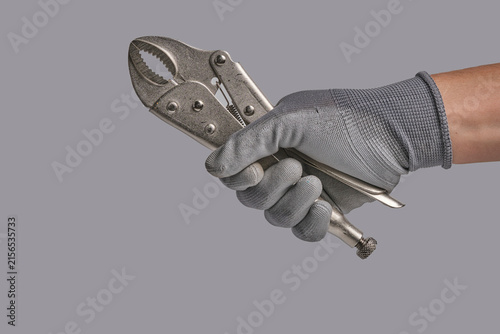 Hand in protective grey glove holding metallic locking pliers isolated against grey studio background.