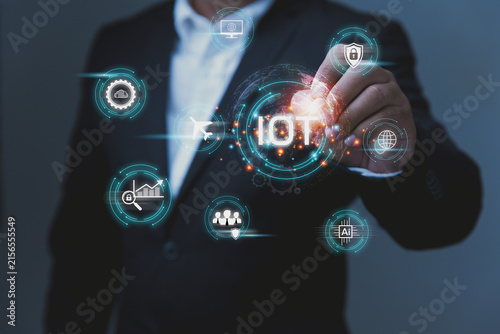 A businessman interacting with an advanced digital interface focused on modern technology. The display highlights the acronym IoT, which stands for the Internet of Things.