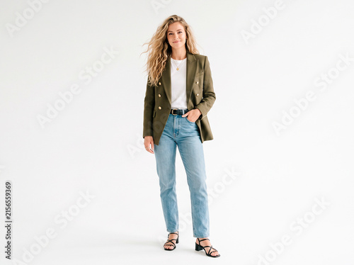Smiling young woman in olive green blazer and jeans posing full length on white background. Successful blonde female model in smart casual outfit, corporate fashion and modern lifestyle portrait