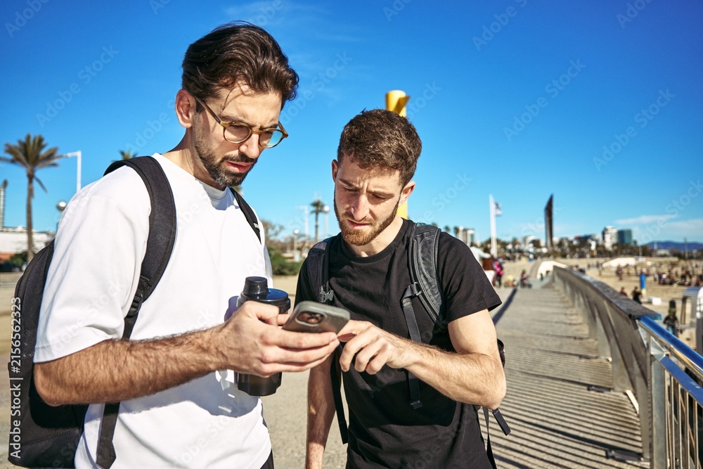 Fototapeta premium Two young athletes using phone while taking part in a recreational game by the beach