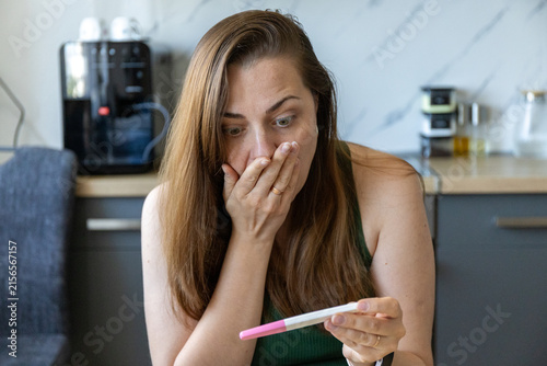 Fotografie Shocked young woman looking at positive pregnancy test at home