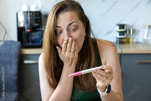 Bild auf Leinwand Shocked young woman looking at positive pregnancy test at home