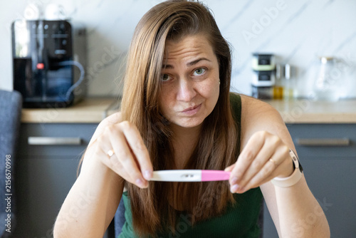 Bild auf Leinwand Unhappy young woman with a positive pregnancy test in her hand at home