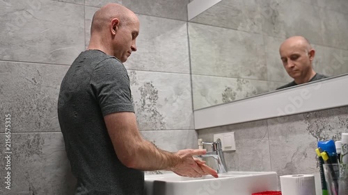 Bald man washing his hands with soap and water in the bathroom for hygiene and virus prevention