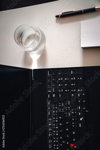 Minimalist professional workspace featuring a laptop keyboard, pen, notebook, and glass of water, conveying productivity and focused work in a clean office setting.