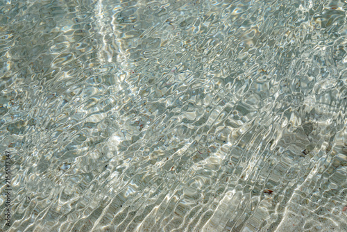 Sunlight creates intricate ripples and reflections across clear shallow water and a sandy bottom, offering a versatile natural texture for environmental and lifestyle designs.