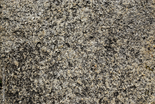Close-up of a naturally weathered rock surface with coarse mineral grains and irregular gray-beige patterns, providing a rugged neutral texture for architectural, design, and background applications.
