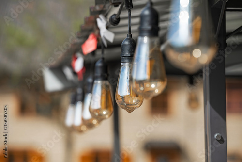 Close up of vintage Edison string lights hanging outdoors during daytime. Decorative unlit patio illumination with shallow depth of field in Latvia.